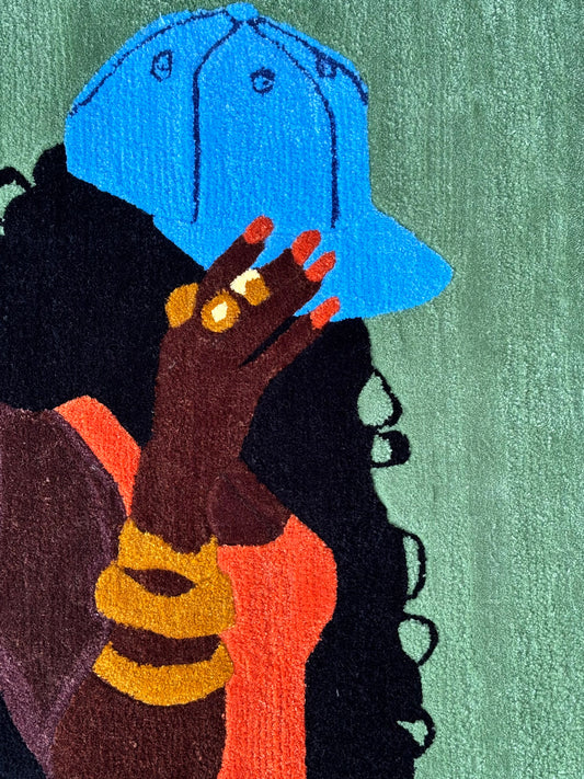 A rug showing a woman in profile wearing a bright blue cap, with dark curly hair, a coral-orange top, gold rings, and a green textured background.
